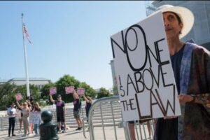 Protester outside the US Supreme Court holding a sign reading "NOELABOVE LAW" during a rally over migrant deportations.